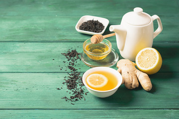 Tea lemon ginger with honey in a white cup and a teapot on a wooden rustic background. Healthy drink for detox health.