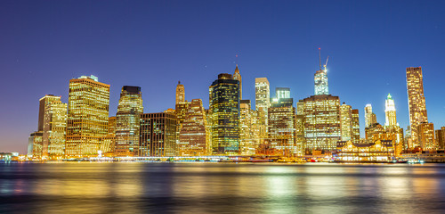 Downtown Manhattan at night from Brooklyn Bridge Park. New York City skyscrapers reflections in the...