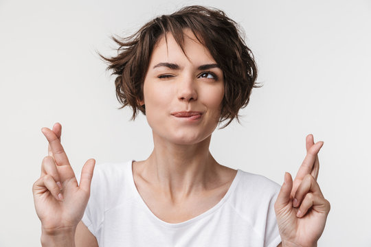 Portrait of cheerful woman with short brown hair in basic t-shirt keeping fingers crossed and wishing good fortune