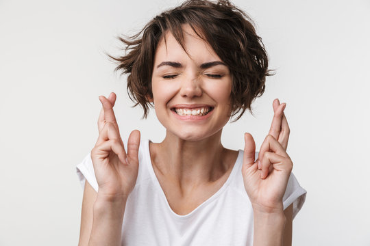 Portrait of attractive woman with short brown hair in basic t-shirt keeping fingers crossed and wishing good fortune