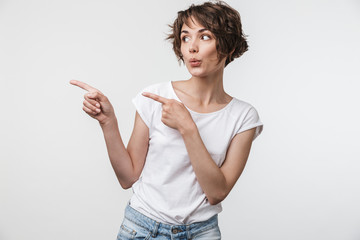 Portrait of young woman with short brown hair in basic t-shirt rejoicing and pointing fingers at copyspace