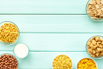 Various corn cereals in bowls and milk on mint wooden background top view copyspace
