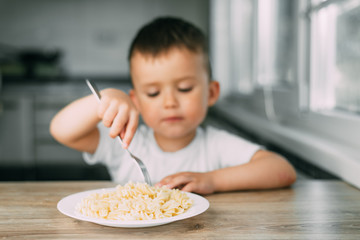 little boy eats pasta in the form of a spiral in the afternoon in the kitchen on their own