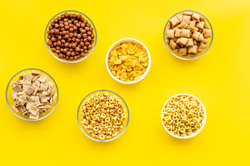 Various corn cereals in bowls on yellow background top view pattern