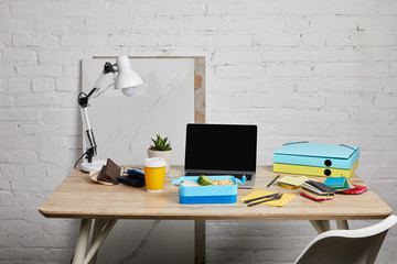 lunch box at workplace with laptop and papers on wooden table on white background, illustrative editorial
