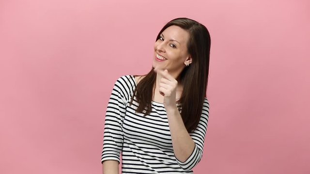 Smiling confident young woman in striped shirt looking camera with charming smile, pointing fingers on herself isolated over pastel pink background in studio. People sincere emotions lifestyle concept
