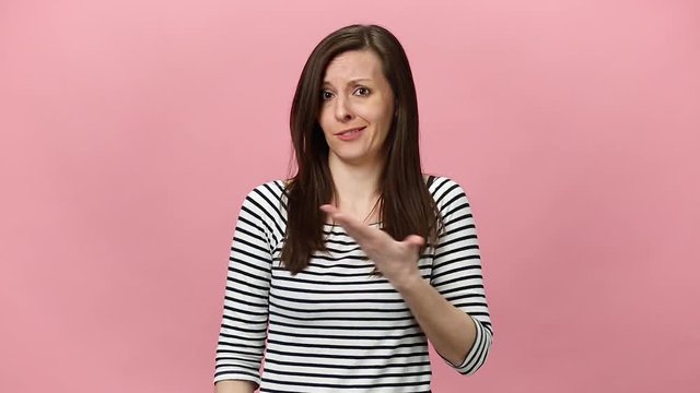 Perplexed pretty confused pensive brunette young woman in striped shirt looking camera, aside, gesticulating isolated over pastel pink background in studio. People sincere emotions, lifestyle concept.