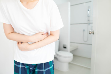 Young female suffering form abdominal pain in front of toilet at home. Causes of abdominal pain...