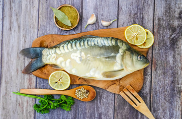 Mirror carp on a cutting Board surrounded by vegetables. Fresh fish before cooking. Fish and vegetables.