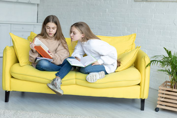 Two little sisters in casual clothes sitting together on yellow sofa