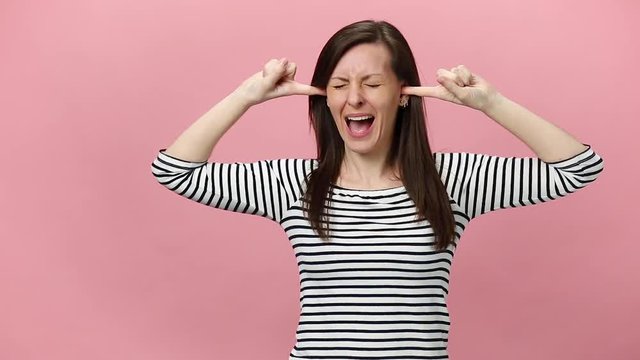 Irritated dissatisfied brunette young woman in striped shirt looking camera gesticulating say no bla-bla-bla isolated over pastel pink background in studio. People sincere emotions, lifestyle concept.