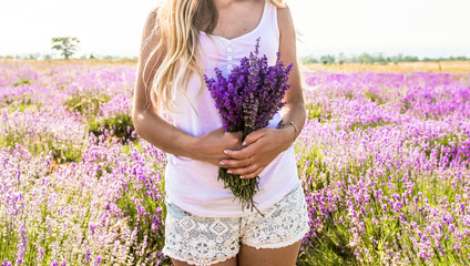 A girl in a white t-shirt and shorts with a bouquet in her hands stands on a lavender field