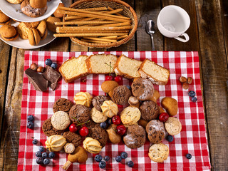 Cookies biscuit with blueberry. Chocolate bake and cherry cupcake with cup tea or coffee and tier stand on kitchen gingham checkered cotton fabric on wooden table village style for picnic top view.