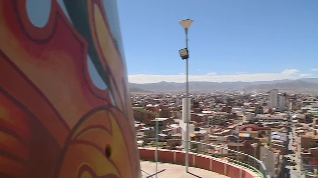 Wide high-angle panning shot of colourful Diablada wall mural painting, and cityscape view from the Sanctuary of Socavon, Oruro, Bolivia