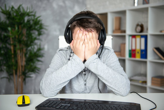 Oops, failure, loss. Teenager boy lost in a computer game. A schoolboy sits upset in front of a computer monitor, covering his face with his hands