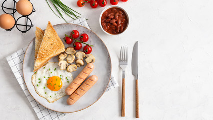 Full English Breakfast including sausages, grilled tomatoes and mushrooms, egg, baked beans and bread. Top view, copy space