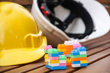 Real estate and new house construction concept. Protective hardhats, and multicoloured plastic construction building blocks or toy bricks. Selective focus