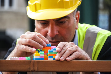 Concentrated civil engineer using multicoloured plastic construction toy building blocks. Outdoors