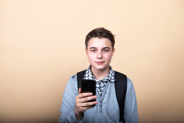smiling teenager guy looking at a cell phone isolated on beige background © Yarkovoy