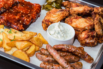 Dish of mixed meats. Grilled ribs, chicken wings and sausages with French fries
