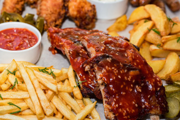 Dish of mixed meats. Grilled ribs, chicken wings and sausages with French fries