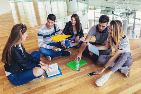 Fellow students sitting on floor in campus and preparing together for exams