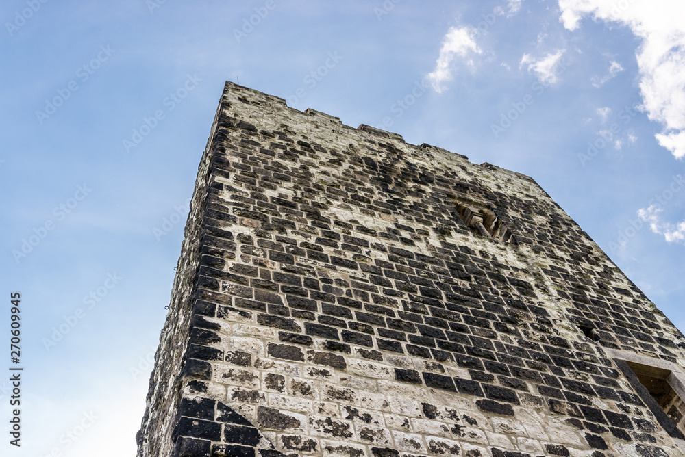 Wall mural The ruins of a historical tower against a blue sky with white clouds.