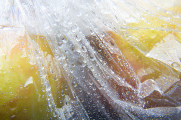 Bolsa de plástico en la cual hay dos manzanas, la bolsa está llena de gotas de agua
