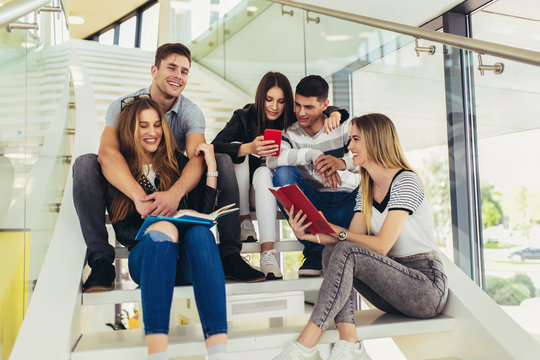 College life.Students are studying in library. Young people are spending time together. Reading book and communicating while sitting on stairs in library.