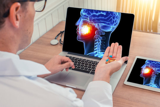 Doctor or dentist holding pills with x-ray of 3D skull head with pain in the teeth on a laptop. Digital tablet on the wooden desk
