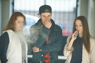 Vape teenagers. Two young cute girls in casual clothes smoke electronic cigarettes near nonsmoking...