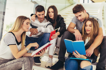 College life.Students are studying in library. Young people are spending time together. Reading book and communicating while sitting on stairs in library.