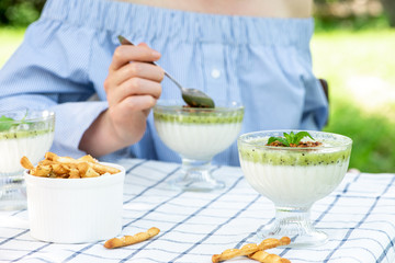 Girl at the garden table with a white tablecloth eats a kiwi milk dessert. Breakfast outdoors.