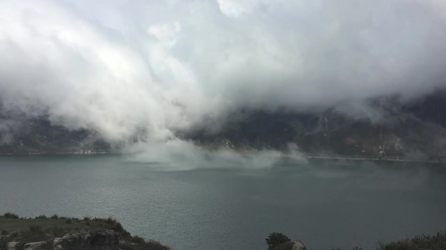View of Quilotoa Lake, an ancient volcano and starting point for the Quilotoa Loop hike with mist close to the green water