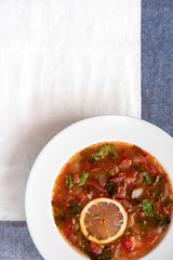 Cold tomato soup with lemon in a white plate on a blue striped towel. Moroccan food. Top view.