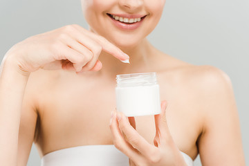 cropped view of smiling woman holding container with face cream isolated on grey