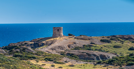 Fototapeta na wymiar Catalan defense tower along the spectacular coastal road between Alghero and Bossa (SP 105), Sardinia, Italy. One of the most panoramic spots in Italy.