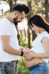 Pregnant woman and her beaeded husband hugging on the tummy together in nature outdoor