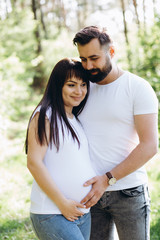 Pregnant woman and her beaeded husband hugging on the tummy together in nature outdoor