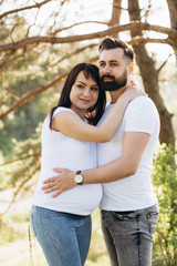 Fototapeta premium Pregnant woman and her beaeded husband hugging on the tummy together in nature outdoor
