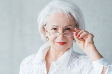 Senior lady portrait. Confident elderly female looking intently over glasses. Curious evaluative self assured business woman.