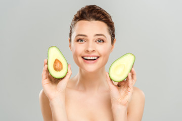 happy naked woman holding halves of organic avocado isolated on grey