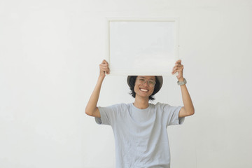 young asian man with glasses and hat holding white board and smiling at camera