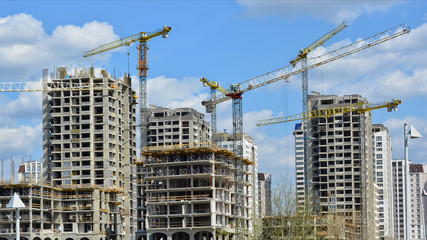 Fototapeta na wymiar Construction site. Big industrial tower cranes with unfinished high raised buildings and blue sky in background. Scaffold. Modern civil engineering. Contemporary urban landscape.