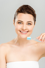 cheerful  woman smiling while holding toothbrush with toothpaste isolated on grey