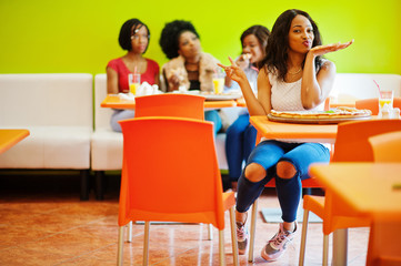 African woman with pizza sitting at restaurant against dark skinned girls.