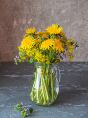 A bouquet of the first primroses in a glass jug. Blooming yellow dandelions, canola and sprigs of mint.