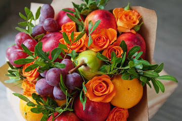 Bouquet of fruits and flowers. Green pear, nectarine, red grapes, orange rose, pistachio, orange. Gray wooden background.