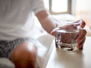 Hand of man holding a clear glass of water for drinking on bed in the Morning