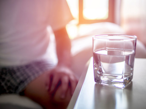 Close Up Photo Glass Of Water On Bedside Table Man Sitting In Bed